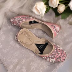 two pairs of shoes sitting on top of a bed next to white roses and flowers