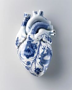 a blue and white heart shaped vase with animals on it's side, against a gray background