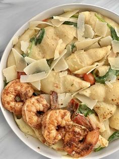 a bowl filled with pasta and shrimp on top of a white countertop next to a fork