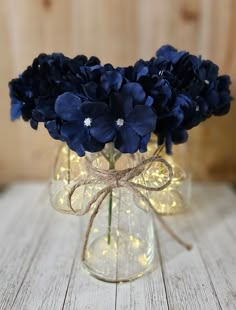 blue flowers in a clear glass vase on a white wooden table with string and lights