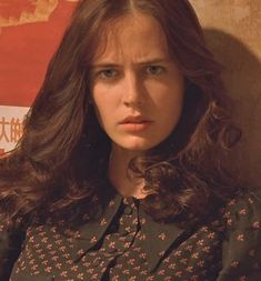 a woman with long brown hair wearing a black shirt and standing in front of a wall