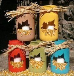 four jars with corn in them are sitting on the ground next to some hay and straw