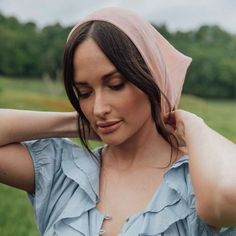 a woman in a blue shirt is wearing a pink head scarf on her head and looking down