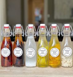 six different types of drinks are lined up on a counter top, with labels in each bottle