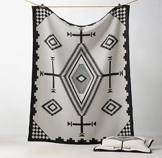 a black and white tapestry hanging on a clothes line with an open book beside it