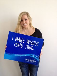 a woman holding a blue sign that says i make wishes come true with water on it