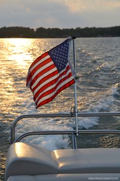 an american flag is waving on the back of a boat in the water at sunset