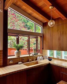 a kitchen with wooden cabinets and tile counter tops, along with a large window that looks out onto the trees outside