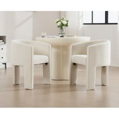 three white chairs around a round table in a room with hardwood flooring and windows