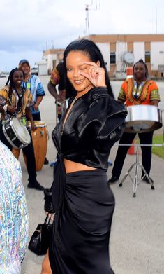 a woman in a black dress is holding her hand up to her face and smiling