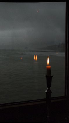 two lit candles sitting on top of a window sill near the ocean at night