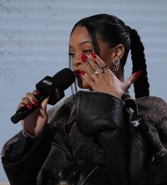 a woman holding a microphone up to her face while wearing red nails and a black jacket