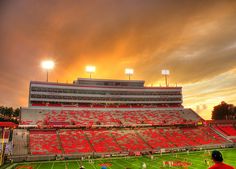 an empty football stadium with the sun setting in the background and people playing on the field