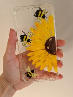 a hand holding a clear case with yellow flowers and bees painted on the back of it