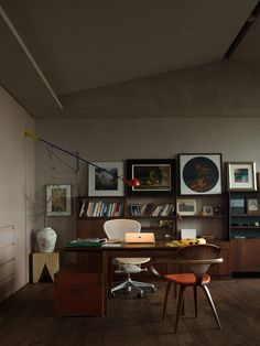 a room with a desk, chair and bookshelf full of pictures on the wall