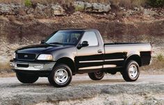 a black pick up truck parked on the side of a road next to some rocks