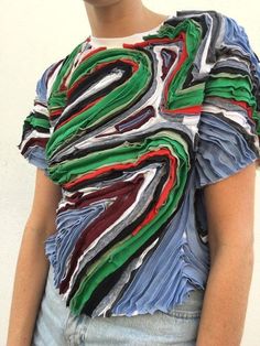 a woman standing in front of a white wall wearing a shirt with multicolored strips on it