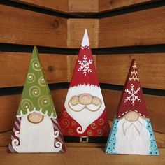 three wooden gnomes sitting next to each other on top of a wood shelf with snowflakes