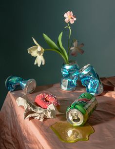 an arrangement of flowers, candy and soda cans on a table with a pink cloth