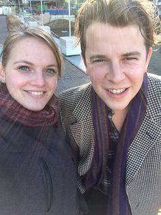 two people standing next to each other smiling at the camera with one person wearing a scarf around his neck