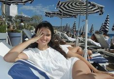 a woman laying on top of a blue and white beach chair next to umbrellas