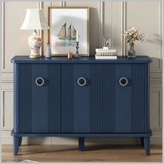 a blue cabinet with two doors and some pictures on it's sideboard next to a lamp