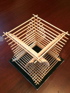 a wooden structure sitting on top of a table next to a black square plate with chopsticks sticking out of it