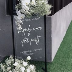 a welcome sign with white flowers and greenery in front of a building on the grass