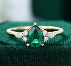 an emerald colored ring with three diamonds on top and green velvet in the back ground