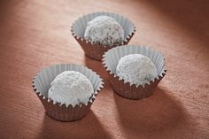 three cupcakes with white frosting sitting on top of a pink tablecloth