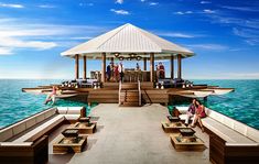 people are sitting on wooden benches at the end of a pier in the middle of the ocean