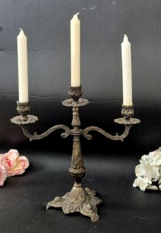 three candles are sitting next to each other on a black surface with flowers in the background