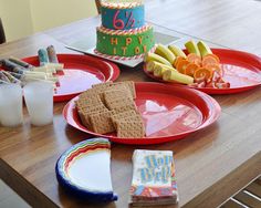 two red plates topped with crackers next to a birthday cake on a wooden table