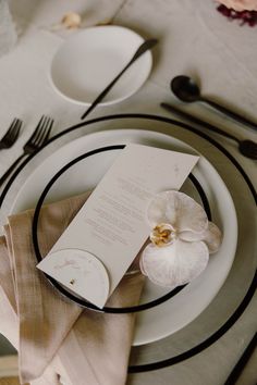 a table setting with white plates and silverware, napkins and an orchid centerpiece