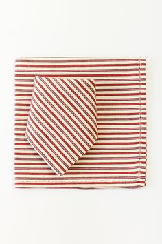 A striped fabric set, including a rectangular placemat and a folded napkin on top. Both the napkin and placemat feature a pattern of alternating red, black, and white horizontal stripes, with the napkin arranged in a diagonal fold that contrasts the direction of the stripes on the placemat. The simple and neat arrangement emphasizes a coordinated, elegant table setting. Bread Warmer, Tuscan Hills, Parlor Games, Get It Together, Holiday Ready, Dinner Napkins, Linen Pillows, Cocktail Napkins, Animal Party