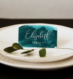 a place card sitting on top of a white plate with green leaves around it and the words elizabeth table 1