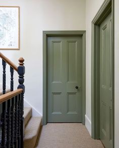 a green door in a white room next to a black bannister and stairs