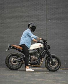 a man riding on the back of a motorcycle down a street next to a brick wall