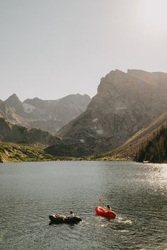 two people are kayaking in the water near mountains