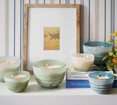 some candles are sitting on a shelf next to books and flowers in vases with pictures behind them