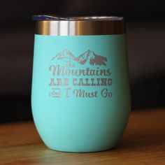 the mountains are calling and i must go engraved tumbler cup on a wooden table