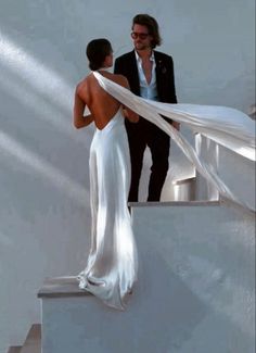 a man and woman are standing on the stairs with their wedding dress blowing in the wind