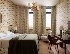 a bedroom with a bed, desk and chair in front of two windows that have floral wallpaper on them