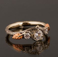 "A delicate, handmade engagement ring made in two gold colors and set with three natural white diamonds of high quality. The grooves in the band are plated with black rhodium which emphasizes the texture. if you prefer not to apply the black rhodium that is fine. I can also use white, rose or yellow gold for the band and the leaves for the same price. The ring in the picture is set with a 0.3ct diamond but can be set with any other stone, please contact me for a quote. Center Diamond - 100% natu Ornate Engagement Rings, Dream Proposal, Handmade Engagement Ring, Gold Twigs, Nature Engagement Ring, Band Ideas, Twig Engagement Ring, Leaf Engagement Ring, Handmade Engagement Rings