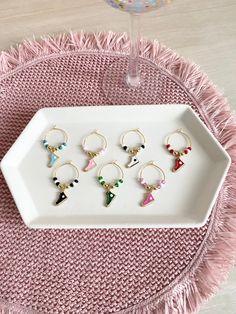 six pairs of earrings sitting on a white tray next to a wine glass and pink table cloth