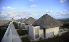 a row of thatched roof houses next to the ocean with blue skies in the background