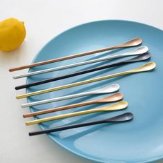 a blue plate topped with lots of silverware next to a yellow lemon and an orange