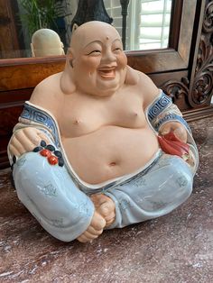 a statue of a laughing buddha sitting on the ground in front of a framed mirror