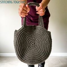 a woman is holding a gray bag made out of knitted yarn and has her hands on the handle