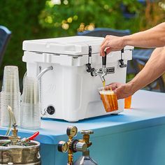 a man is pouring beer into a cooler on a table outside with other items nearby